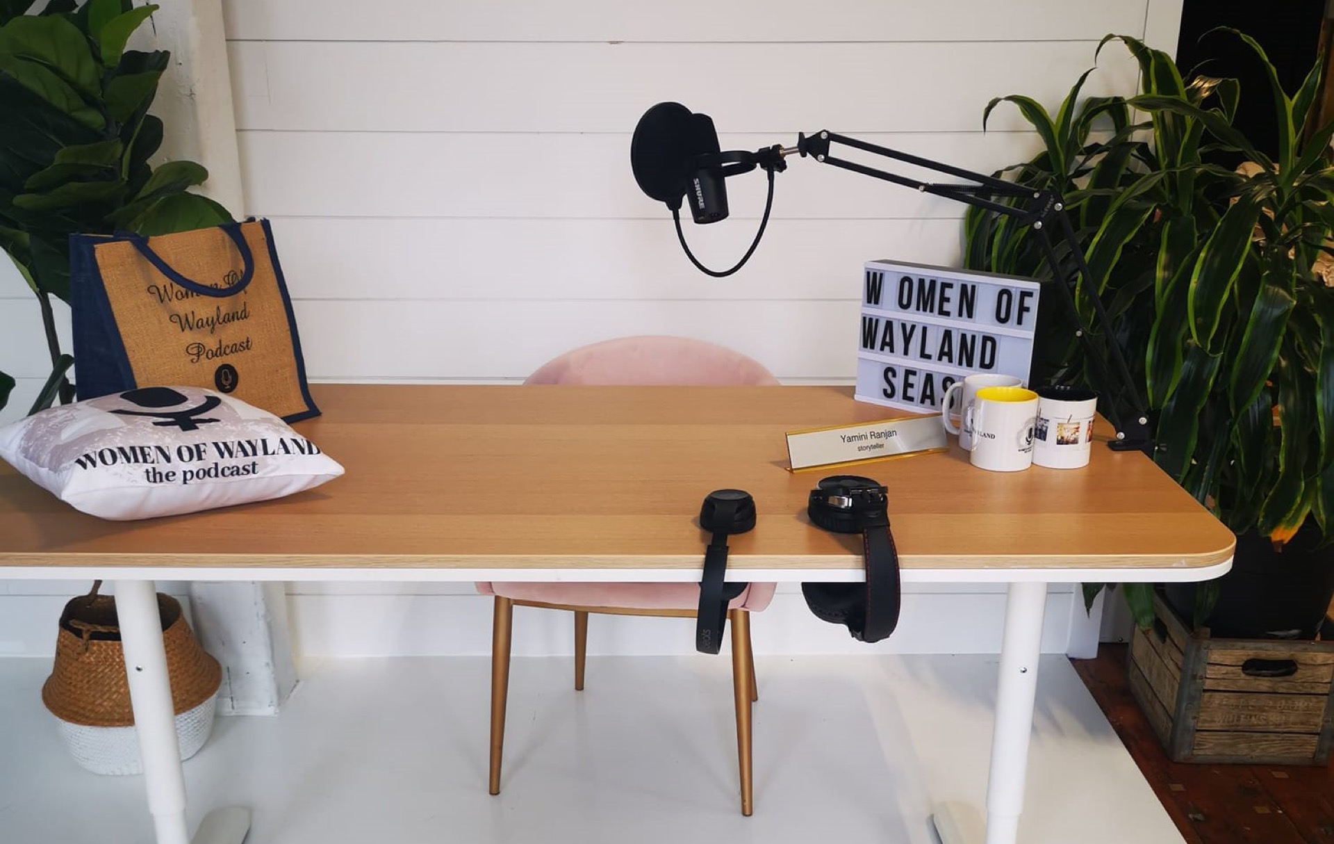 The Women of Wayland podcast studio: a desk with microphones, headphones and a Women of Wayland sign